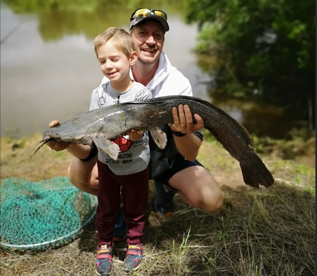 Smiling father and son proudly holding a large catfish caught at Angels Valley fishing