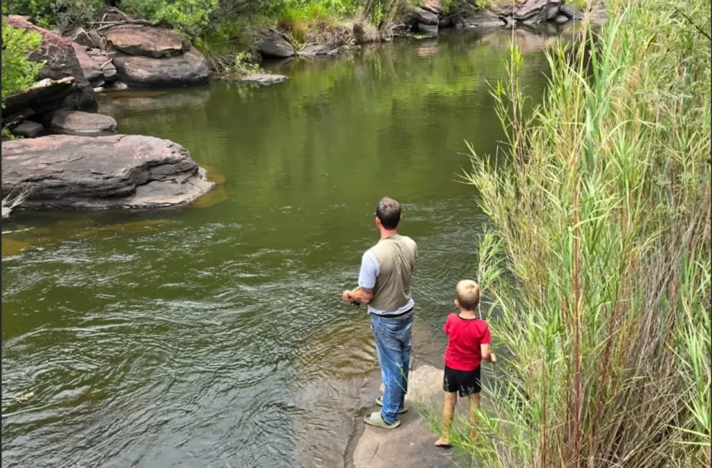 Father and son fishing together at the Wilge River in Angels Valley, surrounded by natural rock and greenery